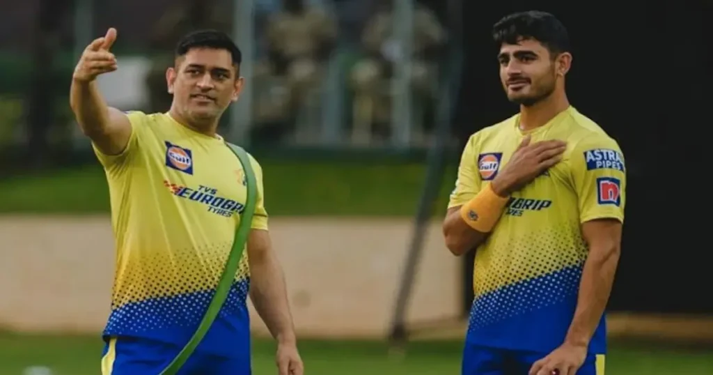 MS Dhoni in his yellow CSK jersey gesturing and offering tactical advice to Mukesh Choudhary during a practice session on a cricket field.