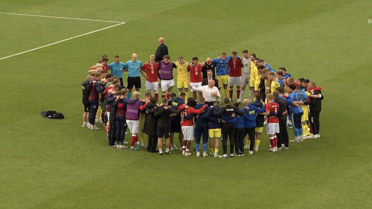 Football players in a tight huddle on the pitch following the Christian Eriksen collapse.